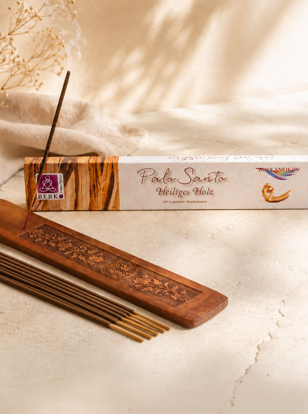 Palo-Santo-Räucherstäbchen mit Verpackung, geschnitztem Holzhalter und glimmendem Räucherstäbchen in einem hellen, warmen Arrangement mit sanftem Sonnenlicht, Leinentuch und dezenter Trockenblumen-Deko.