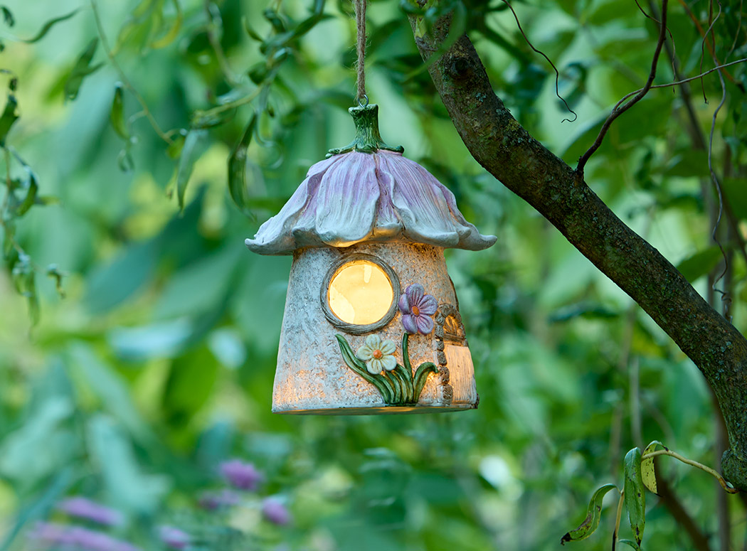 Ein märchenhaftes Solar-Elfenhaus hängt an einem Baumast und leuchtet warm. Umgeben von grünen Blättern entsteht eine verspielte, ruhige Atmosphäre voller Naturverbundenheit und sanfter Geborgenheit.