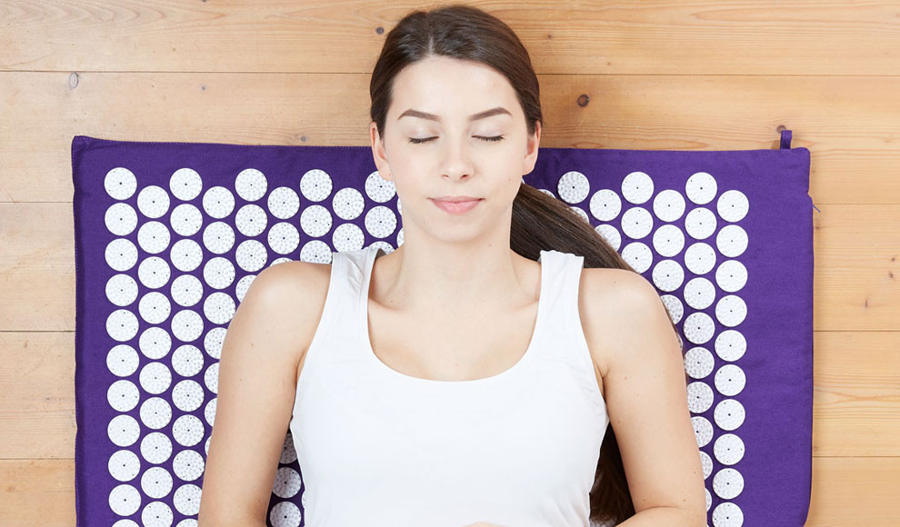 Eine Frau liegt mit geschlossenen Augen und friedlichem Gesichtsausdruck auf einer violetten Akupressur-Matte.