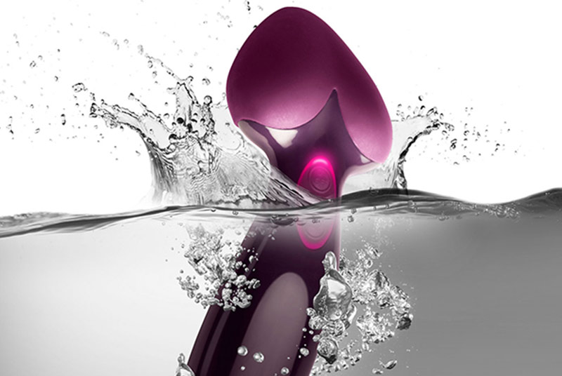 Ein lilafarbener Vibrator mit herzförmiger Spitze taucht im Moment der Aufnahme in Wasser ein.