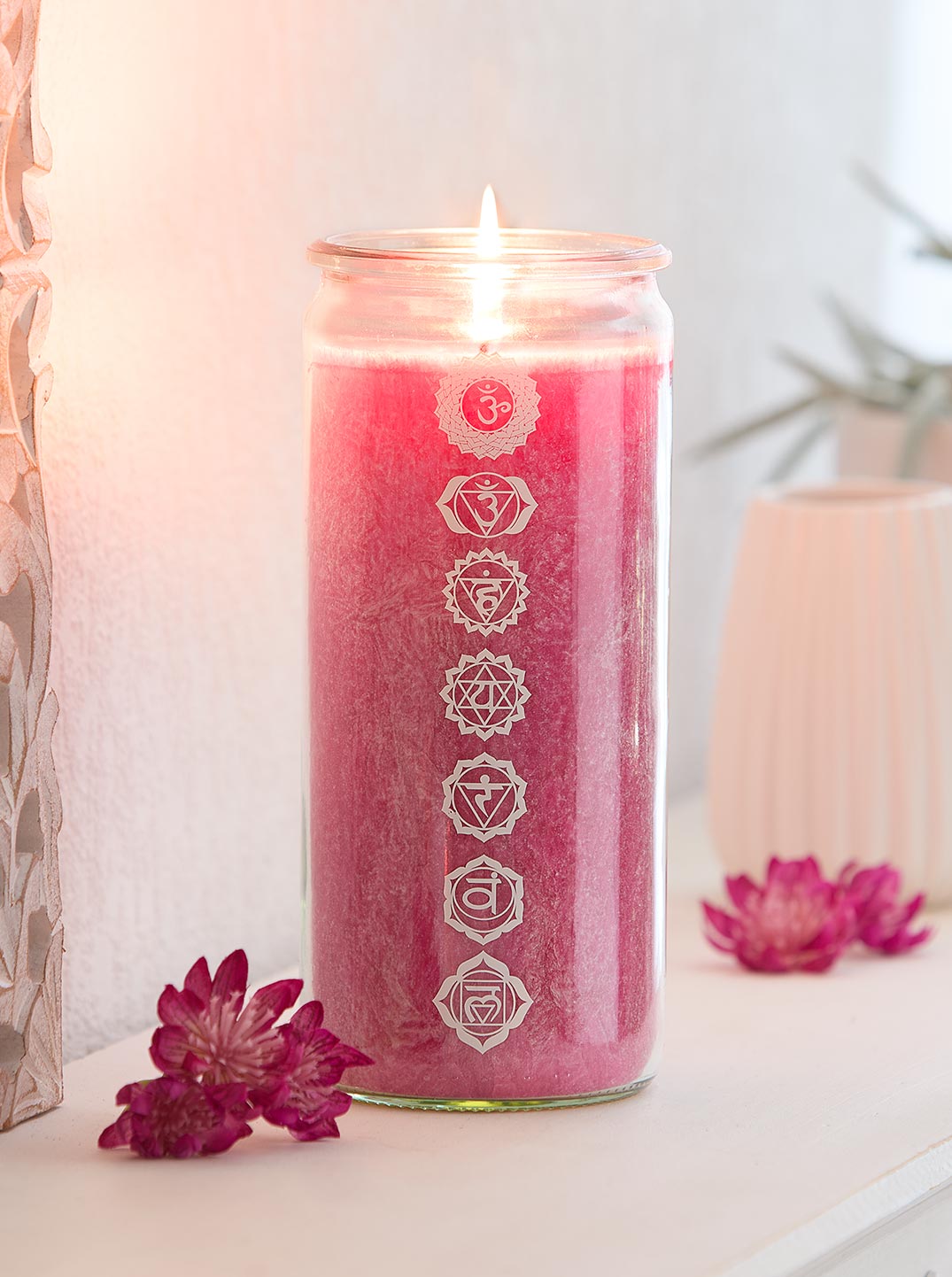 Eine brennende magentafarbene Chakra-Kerze im Glas, bedruckt mit sieben Chakrasymbolen. Im Bild steht: 'Exklusiv bei PranaHaus – Limitierte Auflage'. Die Szene wirkt ruhig und spirituell.