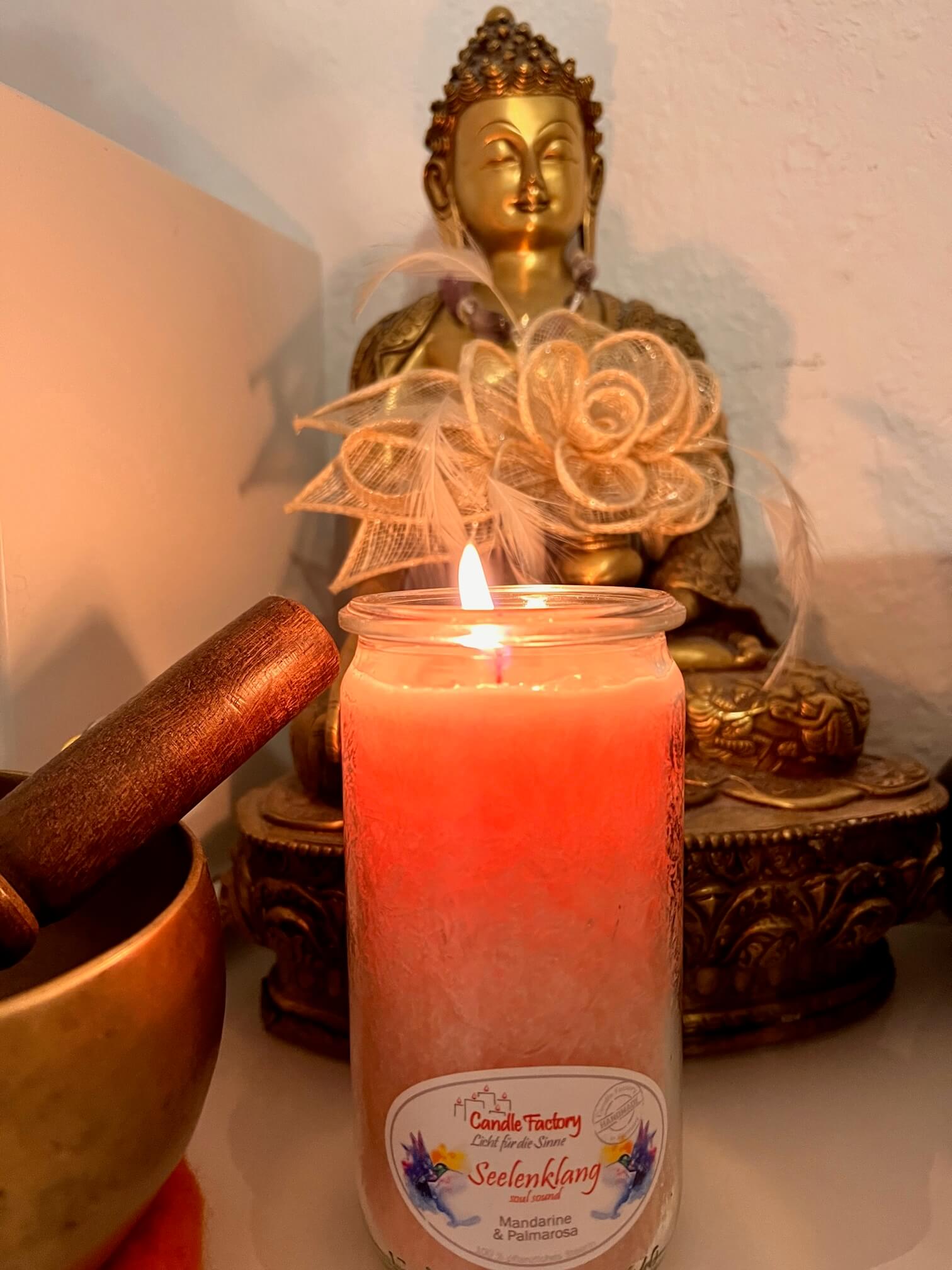 Brennende Kerze vor einer Buddhastatue, daneben eine Klangschale