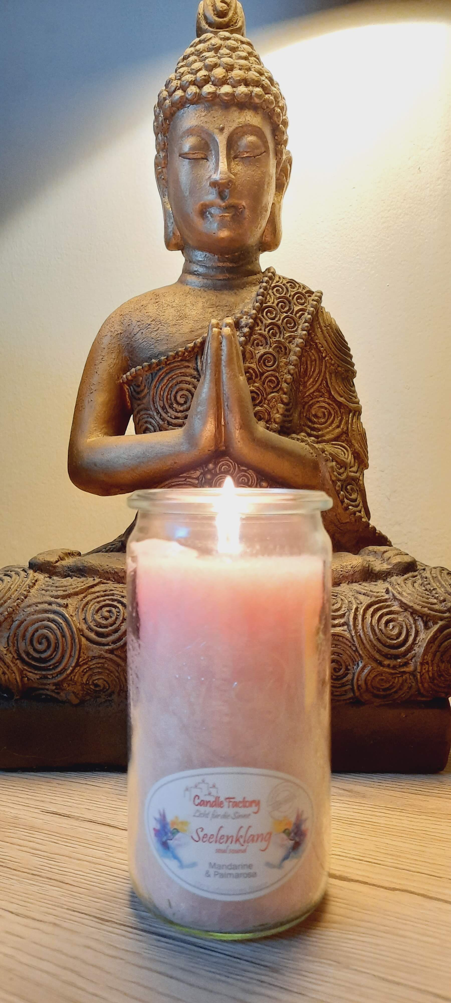 Brennende Kerze vor einer Buddha-Statue im Lotussitz
