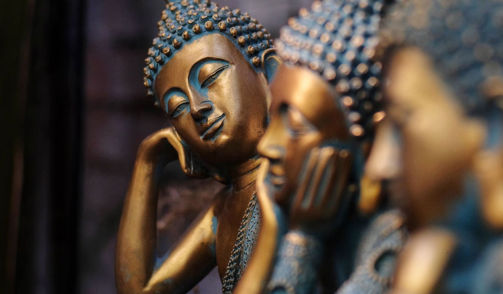Drei goldene Buddha-Statuen in jeweils unterschiedlicher Haltung. Die vordere ist nur unscharf zu erkennen, die zweite hat den Kopf in die Hände gestützt, die dritte neigt den Kopf zur Seite.