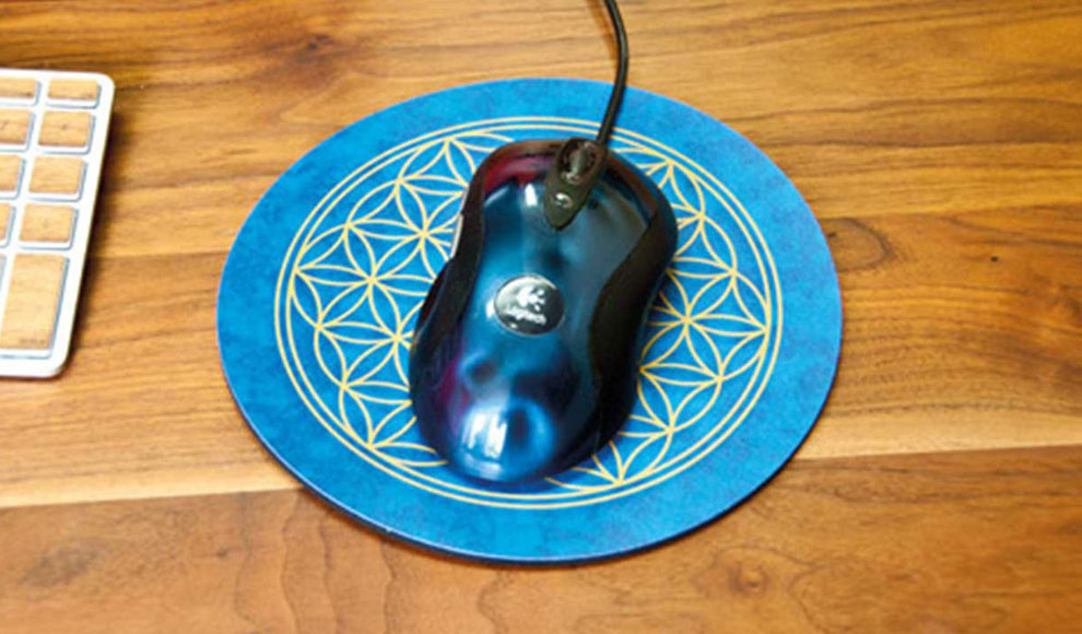 Eine metallic-blaue Computermaus liegt auf einem runden blauen Mousepad, in das golden das Symbol der Blume des Lebens eingeprägt ist