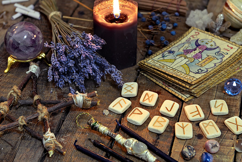 Magische Utensilien: Ein Pentagram aus Ästen, getrocknete Kräuter, Tarotenkarten, Runen und Edelsteine.