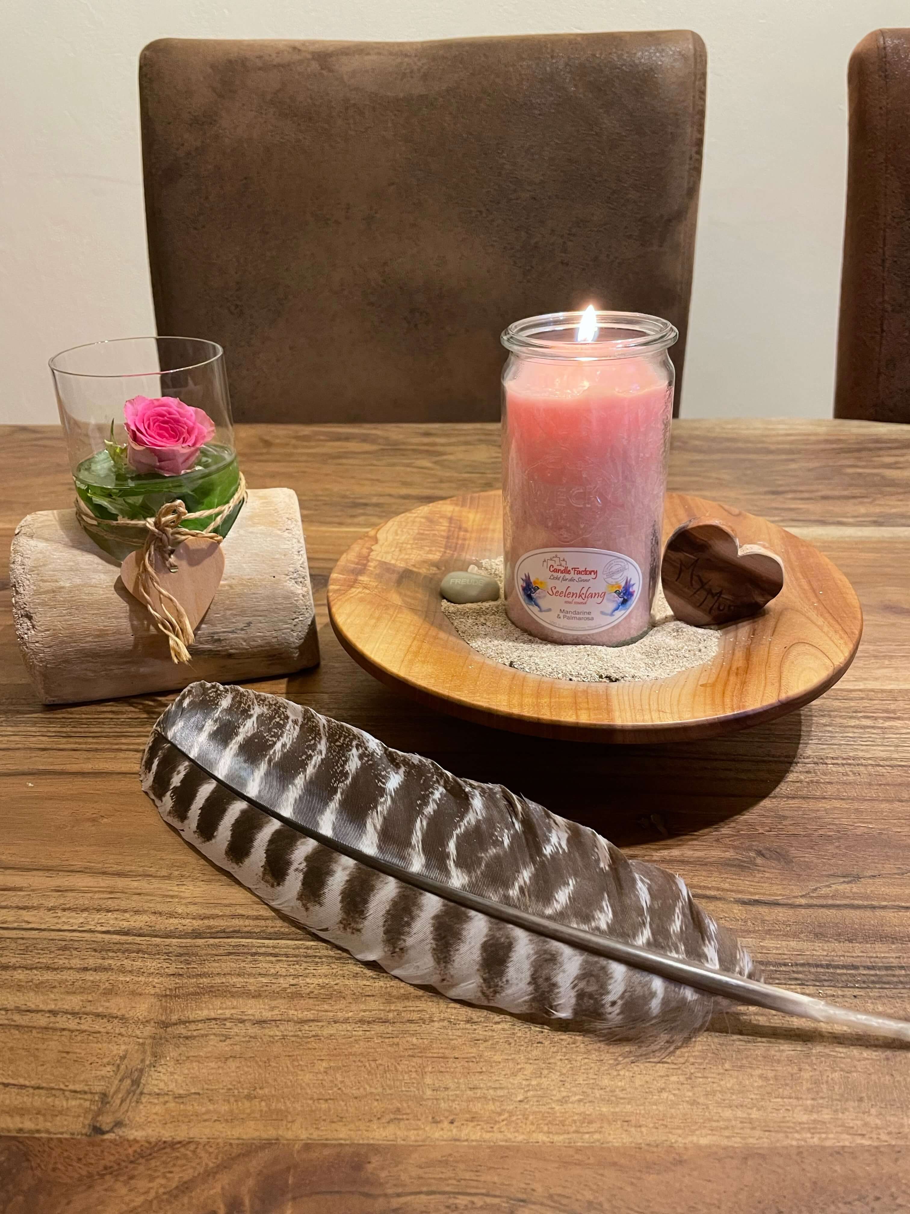 Brennende Kerze in einem Holzteller, dekoriert mit einer Feder