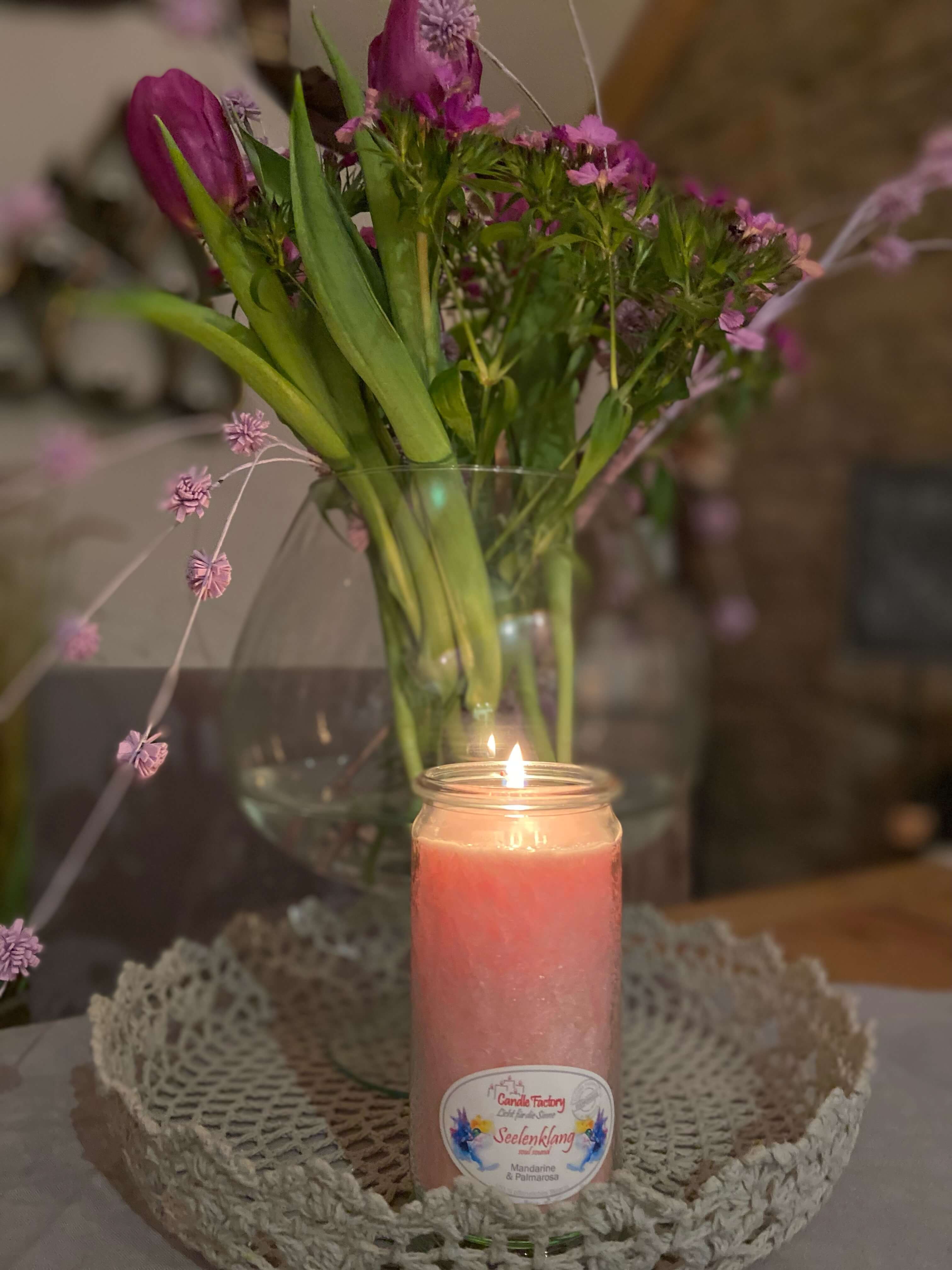 Brennende Kerze vor einer großen Vase mit Frühlingsblumen