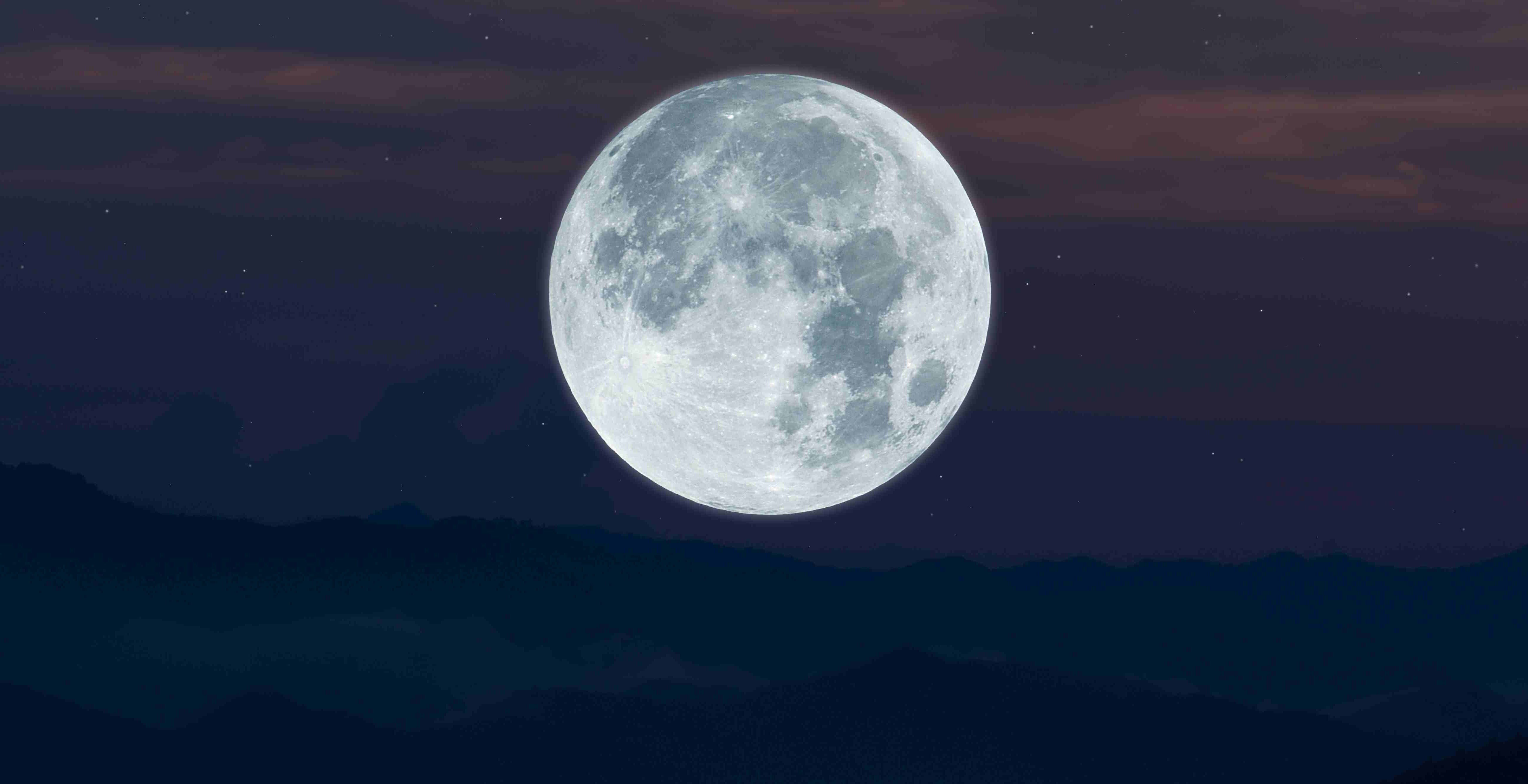 Ein heller Vollmond leuchtet über einer dunklen, bergigen Landschaft bei Nacht.