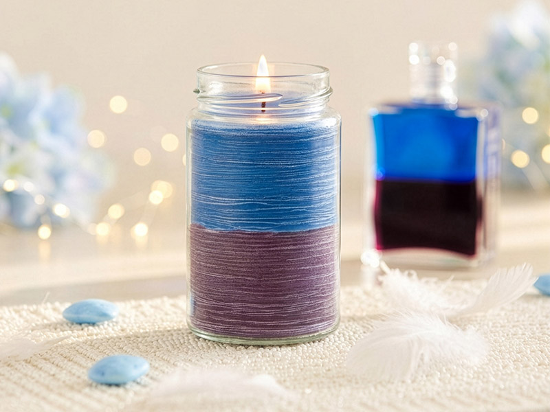 Zweifarbige Duftkerze im Glas in Blau und Violett, sanft brennend vor stimmungsvoller Dekoration. Im Hintergrund die Aura Soma Equilibrium-Flasche B1.