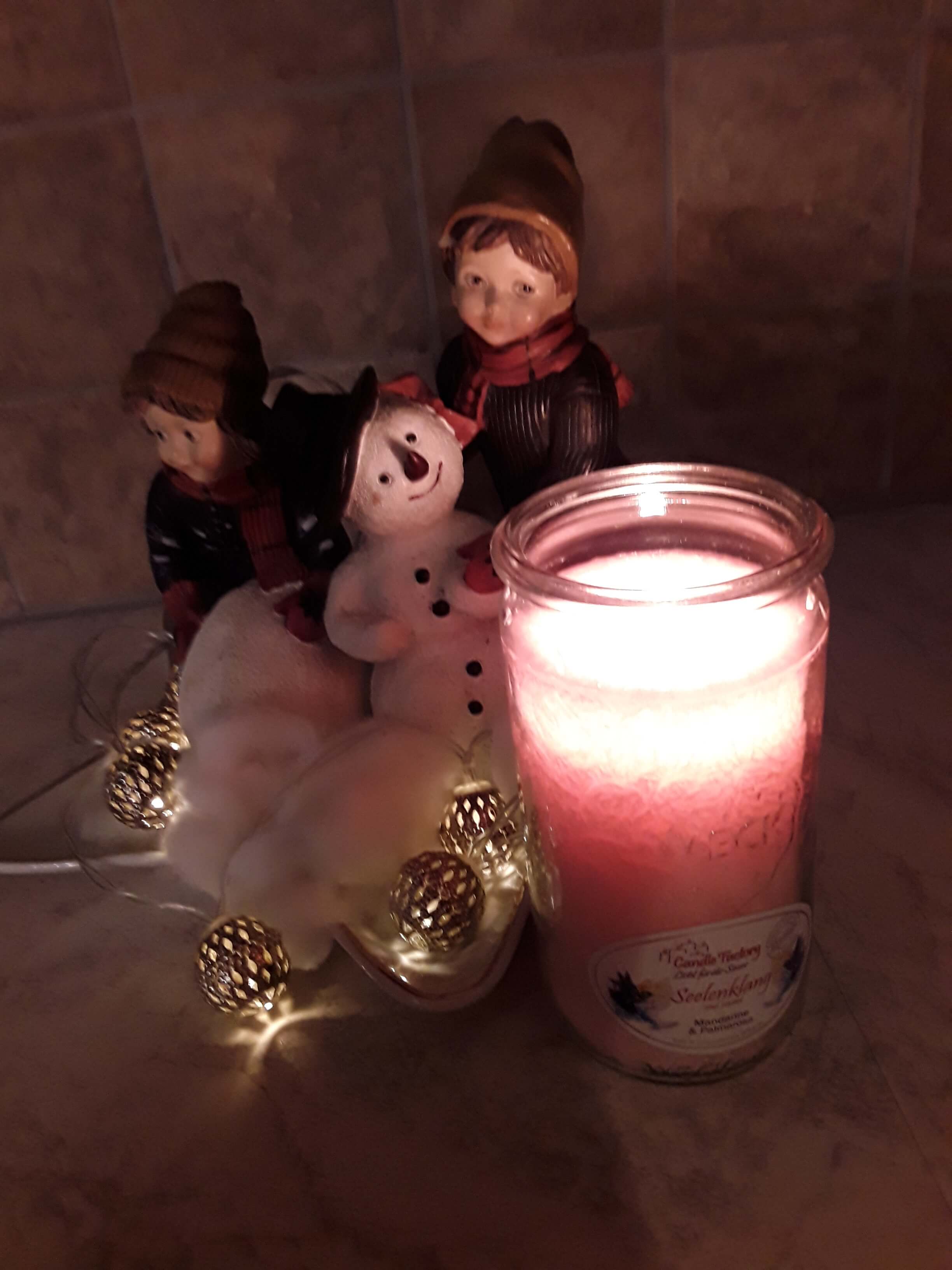 Brennende Kerze neben Figuren von einem Schneemann und zwei Kindern