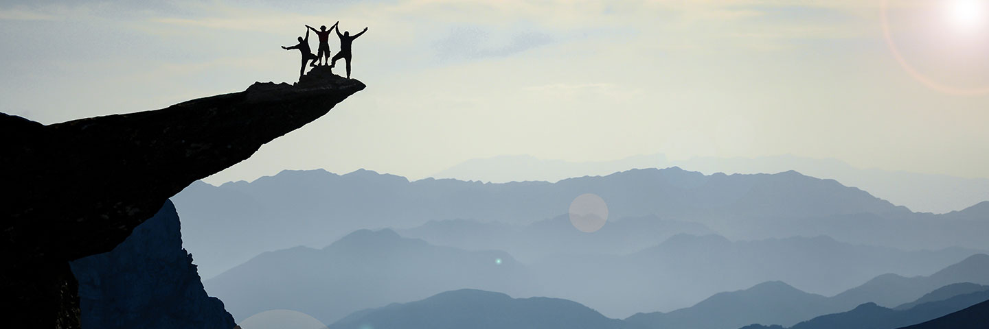 Silhouette eines Teams aus drei Menschen auf einem Felsvorsprung