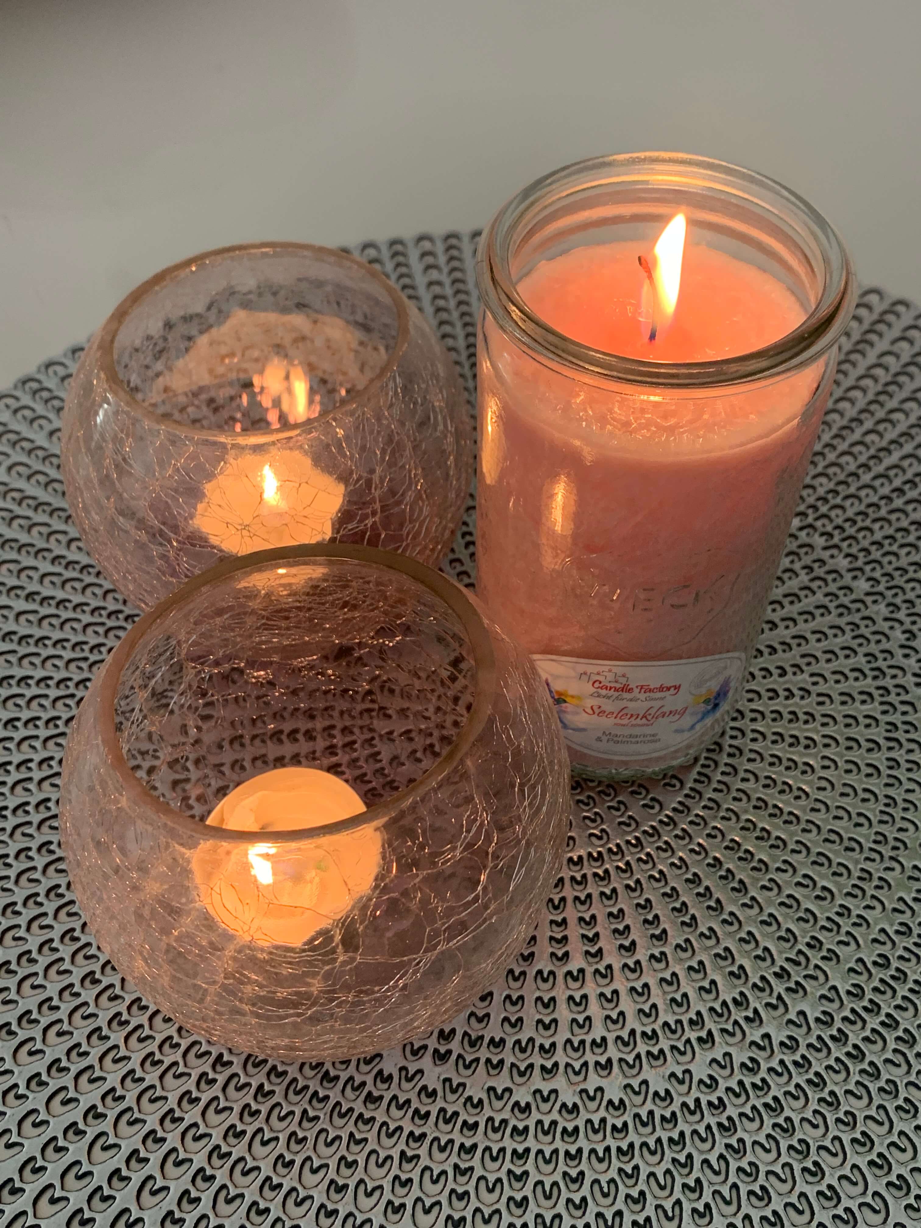 Brennende Kerze im Weckglas neben zwei Teelichtern in kugeligen Windlichtern aus Glas