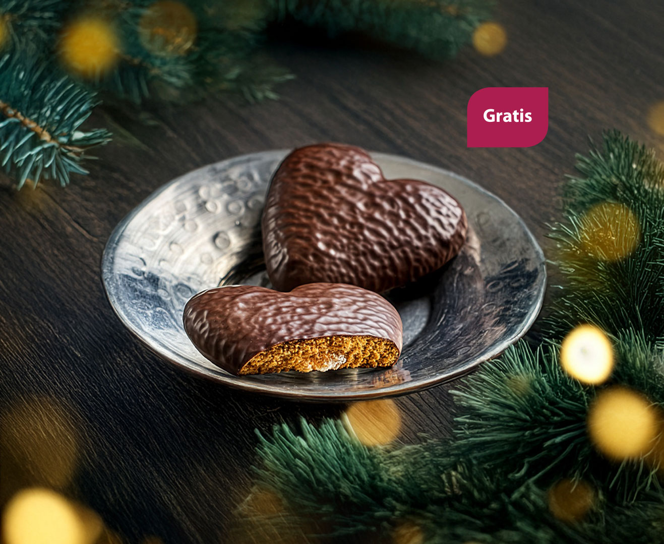 Festliche Szene mit zwei schokolierten Lebkuchen-Herzen in einer silbernen Schale, umrahmt von Tannenzweigen und goldenem Lichterglanz.