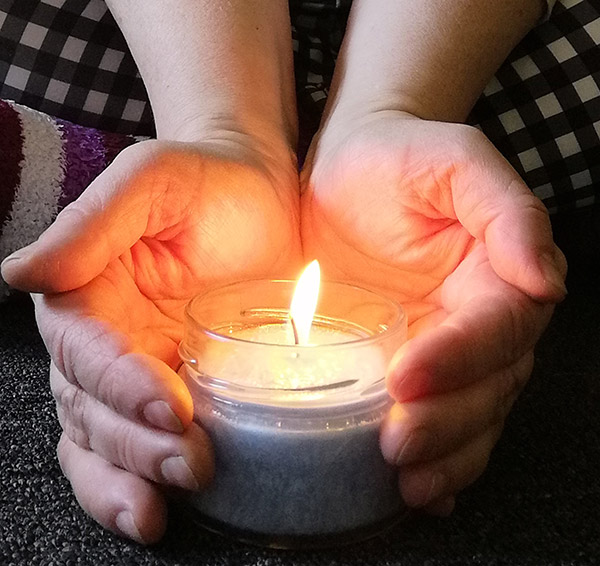 Hände halten schützend die Mini-Duftkerze "Frieden"