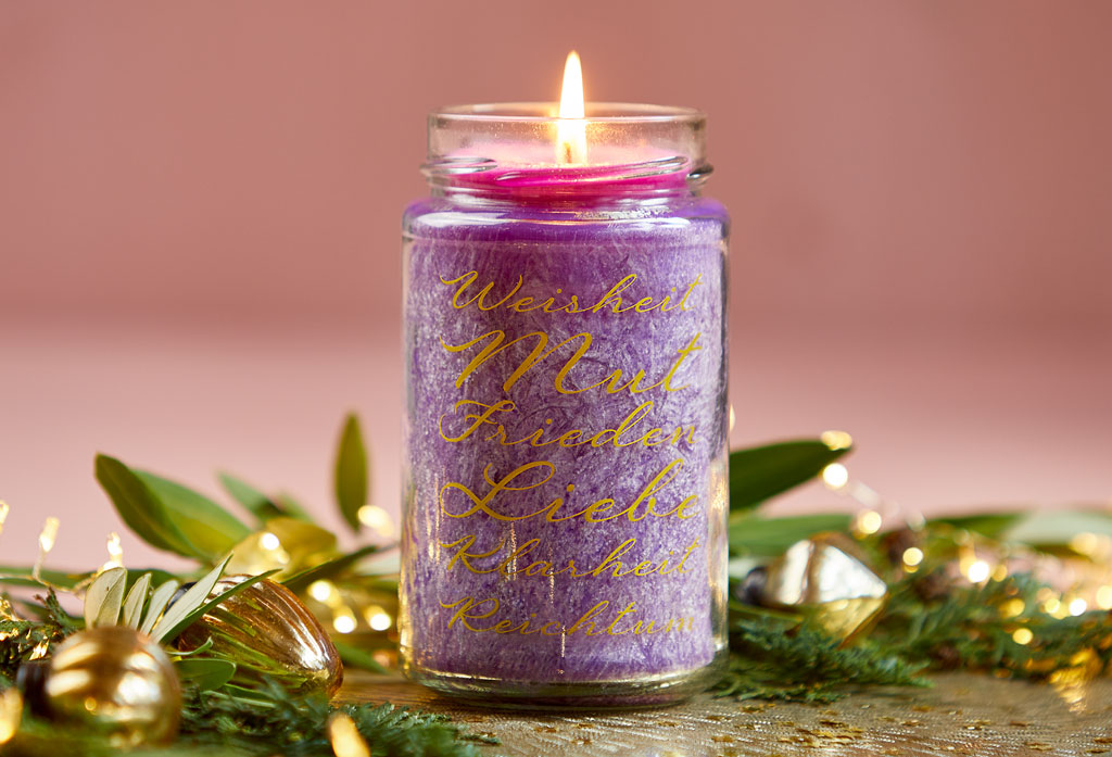 Eine lila Kerze in einem hohen Schraubglas, das mit den goldenen Worten "Weisheit, Mut, Frieden, Liebe, Klarheit und Reichtum" bedruckt ist