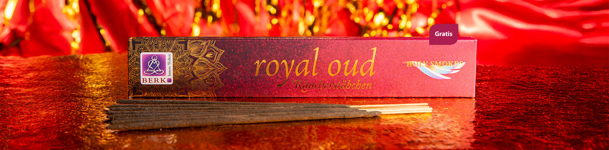 Eine edle Packung Räucherstäbchen der Sorte „Royal Oud“ liegt auf einer glitzernden rot-goldenen Oberfläche. Vor der Verpackung sind mehrere dunkle Räucherstäbchen ausgebreitet.