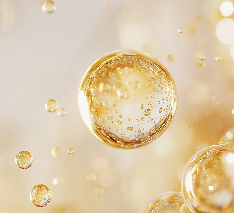 Vergrößerte, schwebende goldene Tropfen mit schimmernden Blattgold-Partikeln, die im Inneren schweben.