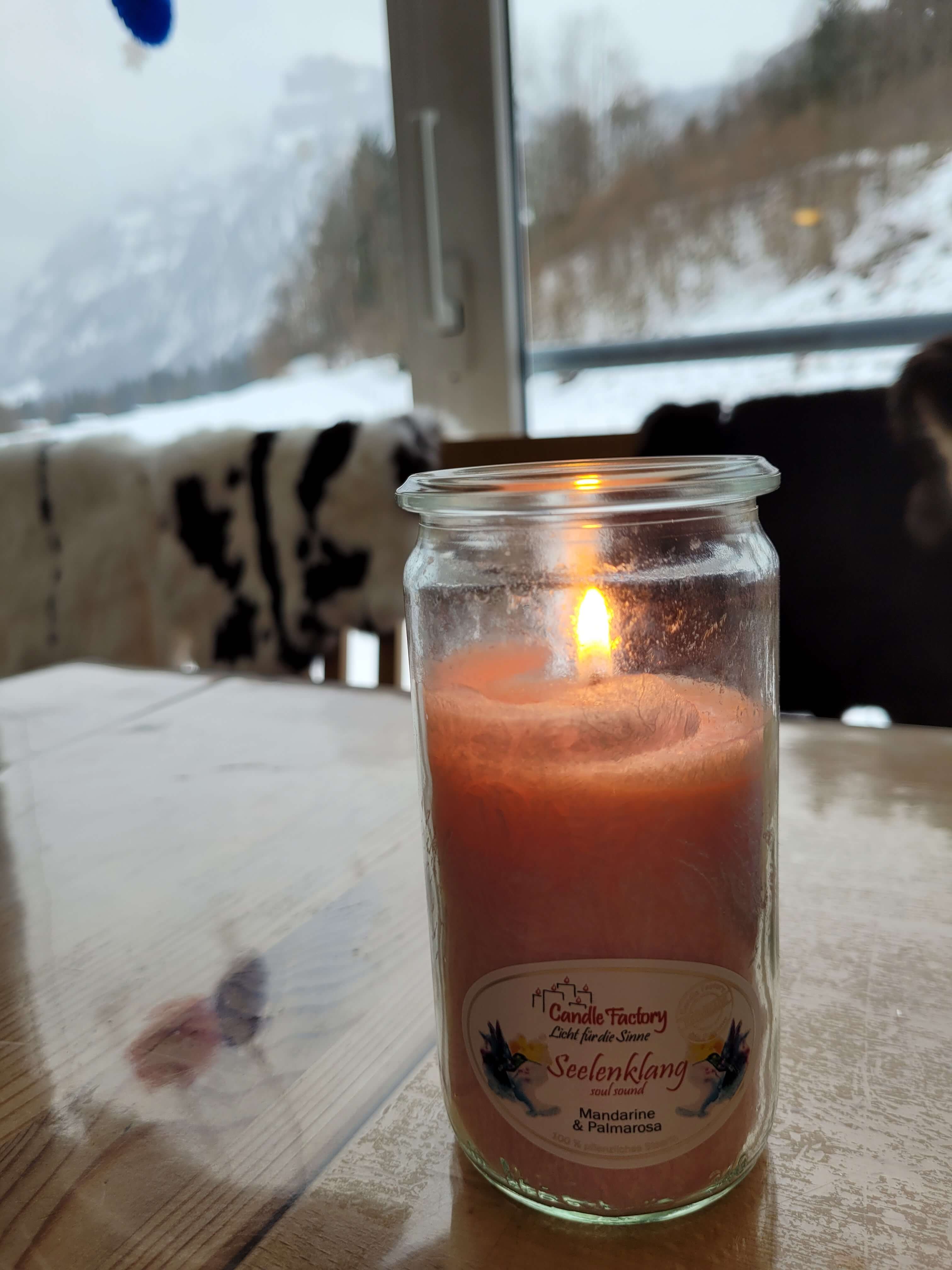 Brennende Kerze auf einem glatt polierten Holztisch vor einem Fenster, draußen liegt Schnee