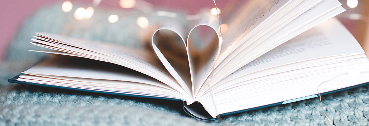 Ein Buch liegt offen auf einer Wolldecke. Zwei Seiten sind so gefaltet, dass sie ein Herz bilden.