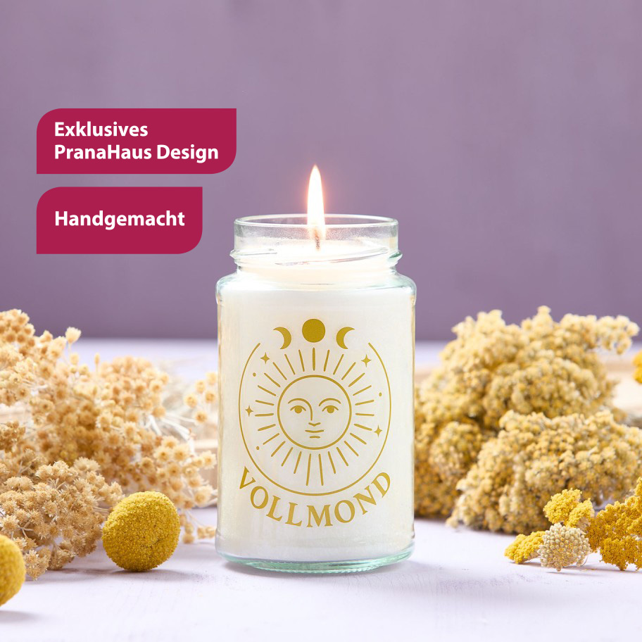 Weiße Duftkerze in einem schlichten Glas mit goldfarbener Sonnen- und Mondsymbolik sowie dem Schriftzug „Vollmond“, liebevoll arrangiert zwischen Trockenblumen.