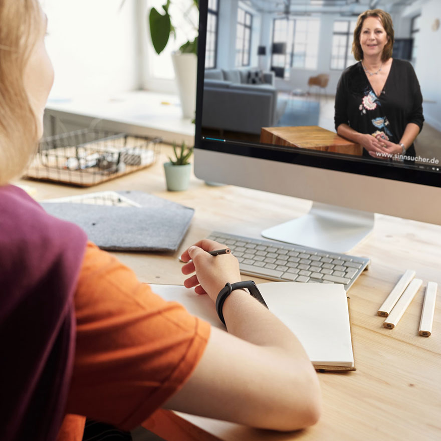 Eine Person sitzt mit dem Rücken zur Kamera vor einem Bildschirm und schaut ein Video zum Online-Kurs mit Stefanie Stahl. Sie hält einen Stift und hat ein Notizbuch bereitgelegt.