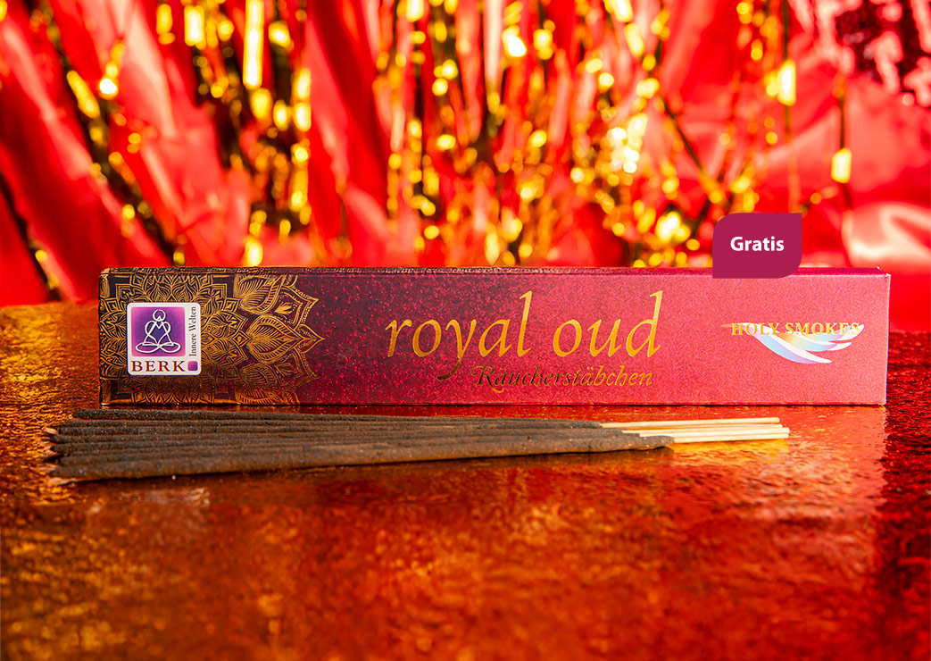 Eine edle Packung Räucherstäbchen der Sorte „Royal Oud“ liegt auf einer glitzernden rot-goldenen Oberfläche. Vor der Verpackung sind mehrere dunkle Räucherstäbchen ausgebreitet.