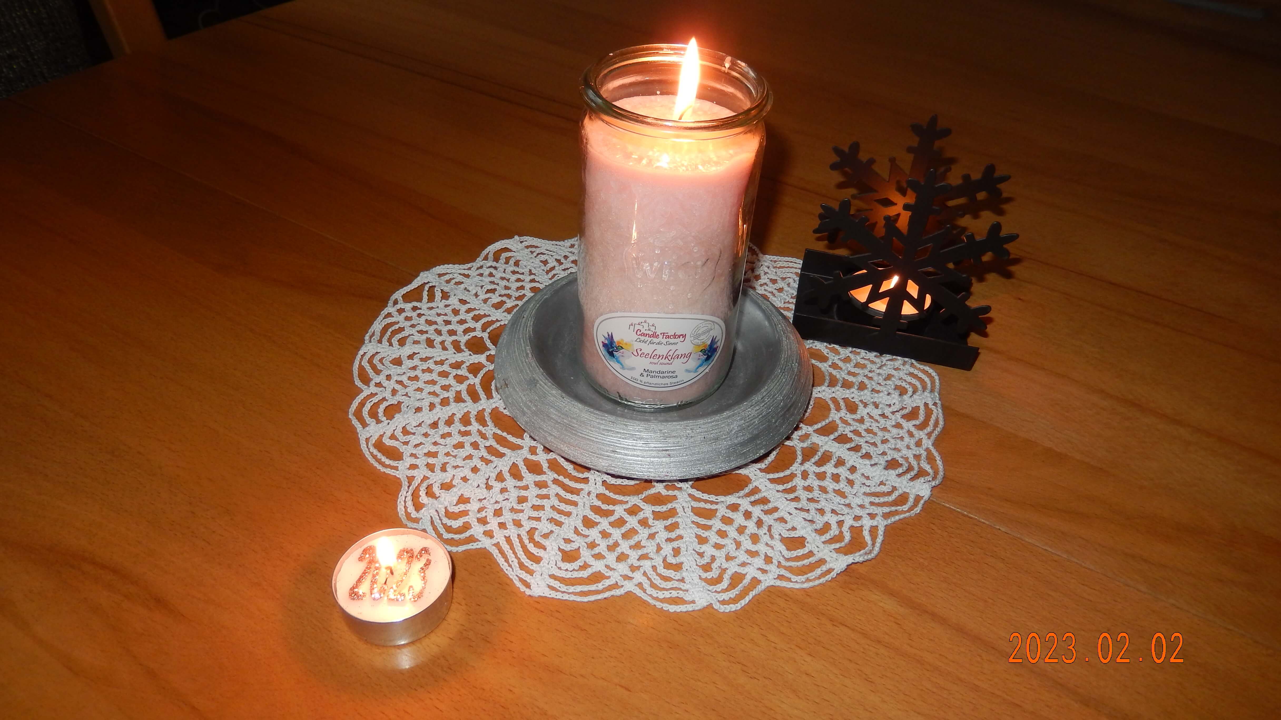 Brennende Kerze auf einem Spitzdeckchen, daneben ein Teelichthalter in Schneeflocken-Form