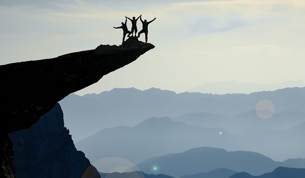 Silhouette eines Teams aus drei Menschen auf einem Felsvorsprung